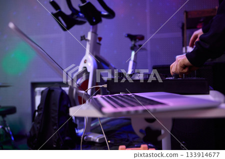 Individual managing broadcast amidst purple lighting and tech equipment, Person programming live stream in subdued purple environment with audio and exercise gear 133914677