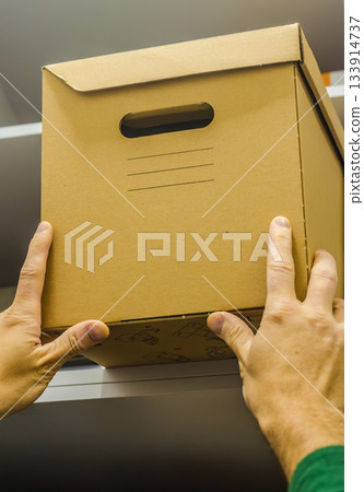Man Lifting Cardboard Storage Box Onto Shelf Man Lifting Cardboard Storage Box Onto Shelf 133914737