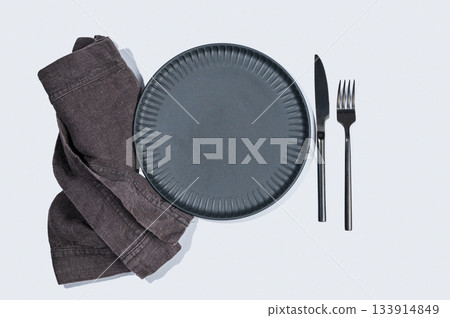 A black textured plate with a fork, knife, and linen napkin on a light background. A black textured plate with a fork, knife, and linen napkin on a light background. 133914849