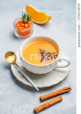 Sea buckthorn herbal tea in a cup on a light background with spices, berries and spoon. 133914859