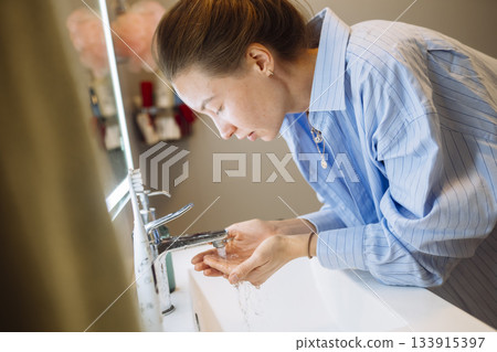 Caucasian woman gently cleansing her face in soft warm light 133915397