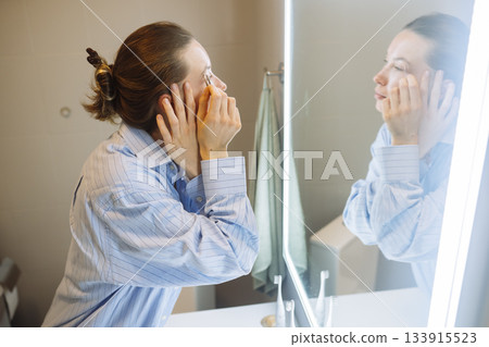 Mirror reflection of woman gently applying cosmetic cream 133915523