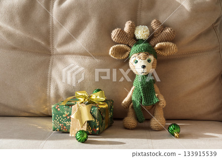 Crocheted Reindeer with Christmas Gift Box and Ornaments on Cozy Holiday Background Crocheted Reindeer with Christmas Gift Box and Ornaments on Cozy Holiday Background 133915539
