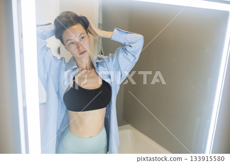Serene morning routine with woman adjusting her hair near bathroom mirror 133915580