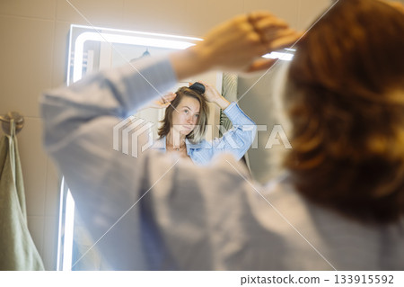 Smiling young woman adjusts hair before busy workday start Smiling young woman adjusts hair before busy workday start 133915592