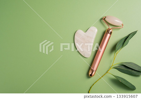 Gua sha tool and face massage roller on green background, beauty abstract photo. Top view. Gua sha tool and face massage roller on green background, beauty abstract photo. Top view. 133915607