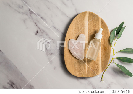 Rose quartz gua sha tool and oil bottle on wooden tray, face massage tool, beauty abstract photo. Copy space 133915646