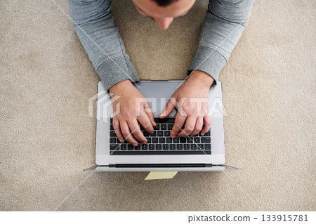 A man working from home on laptop laying down on the floor, top view A man working from home on laptop laying down on the floor, top view 133915781