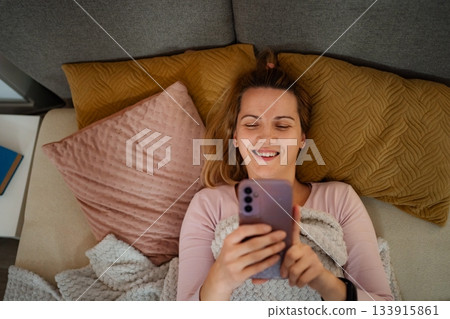 Woman smiling relaxing on couch using smartphone 133915861