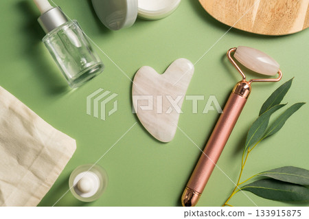 Rose quartz gua sha tool and face massage roller on green background, beauty abstract photo. Top view Rose quartz gua sha tool and face massage roller on green background, beauty abstract photo. Top view 133915875