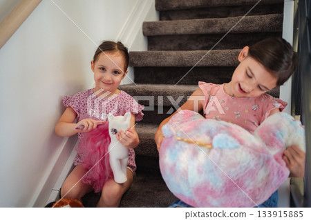 Two sisters playing with their unicorn plushies on the stairs 133915885