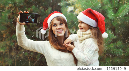 Happy mother and little girl child smiling taking selfie with smartphone near Christmas tree Happy mother and little girl child smiling taking selfie with smartphone near Christmas tree 133915949