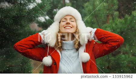 Winter day, happy smiling young woman enjoys snow, warm weather against Christmas tree background Winter day, happy smiling young woman enjoys snow, warm weather against Christmas tree background 133915962