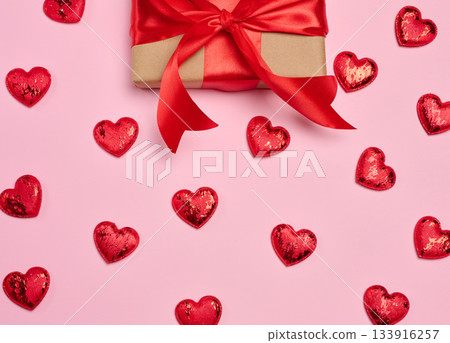 Gift box wrapped in craft paper and tied with a red satin bow on a pink background 133916257