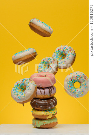 Levitating donuts with sugar sprinkles levitate on a yellow background Levitating donuts with sugar sprinkles levitate on a yellow background 133916273