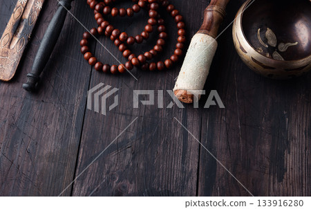 On a wooden background above are traditional meditation items: a Tibetan singing bowl, wooden mala beads 133916280