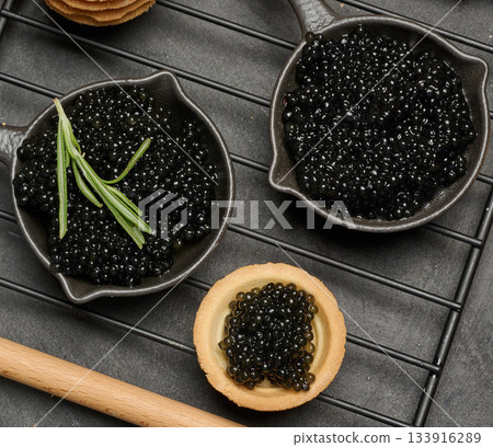 Black caviar in cast iron pans and tartlet on dark board. Top view Black caviar in cast iron pans and tartlet on dark board. Top view 133916289
