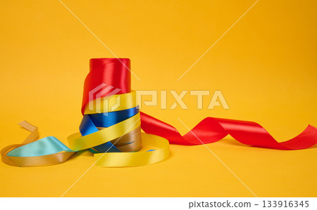 Rolled bright satin ribbons on a yellow background, festive decor Rolled bright satin ribbons on a yellow background, festive decor 133916345