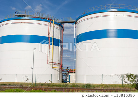 Row many large industrial fuel storage white tanks clear blue sky background on sunny day. Oil storage refinery depot liquid facilities. Energy hazmat railroad transportation storage and distribution 133916390