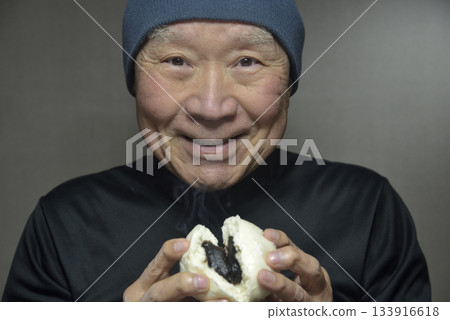 一位老人面帶微笑地吃著熱氣騰騰的豆沙包。 一位老人面帶微笑地吃著熱氣騰騰的豆沙包。 133916618