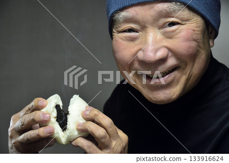 一位老人面帶微笑地吃著熱氣騰騰的豆沙包。 133916624