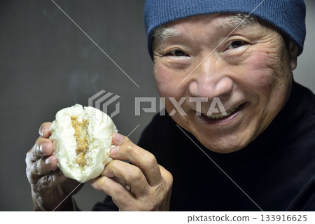 一位老人面帶微笑地吃著熱氣騰騰的包子。 一位老人面帶微笑地吃著熱氣騰騰的包子。 133916625