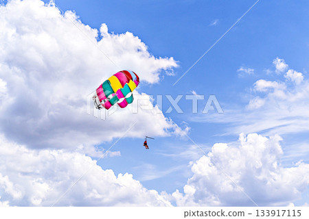 Two people parasailing under a colorful parachute in the sky Two people parasailing under a colorful parachute in the sky 133917115