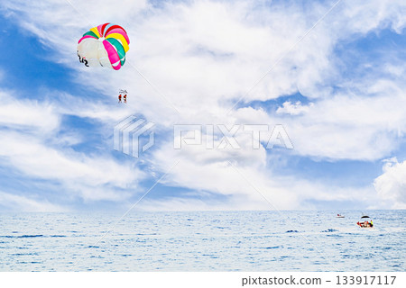 Two people parasailing under a colorful parachute in the sky 133917117