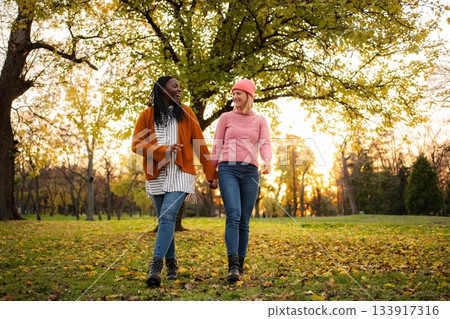 Diverse women friends holding hands walking in autumn park 133917316