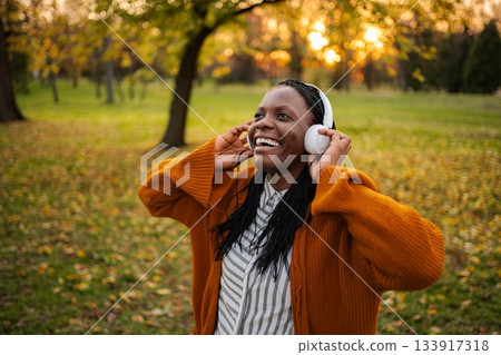 Happy woman enjoying music listening to headphones in park 133917318