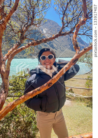 A teen is posing for a picture in front of a tree and a body of water A teen is posing for a picture in front of a tree and a body of water 133917407