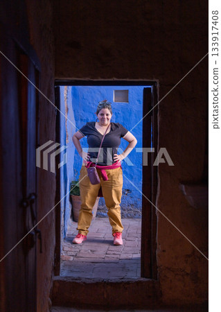 A woman stands in front of a blue door, wearing a black shirt and yellow pants A woman stands in front of a blue door, wearing a black shirt and yellow pants 133917408