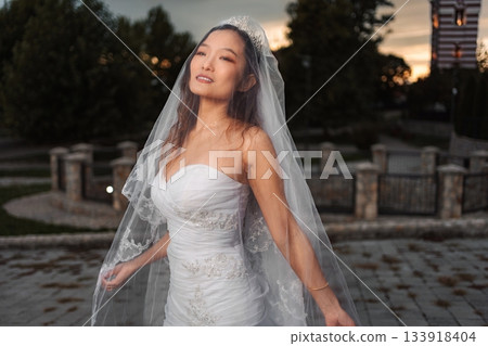 Asian bride wearing wedding dress and veil at sunset Asian bride wearing wedding dress and veil at sunset 133918404