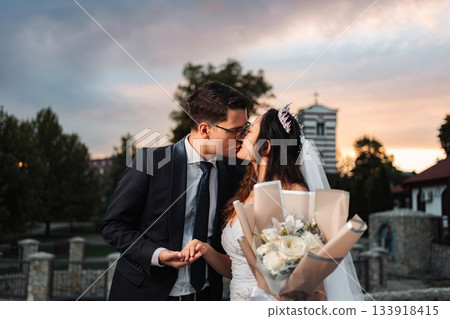 Interracial wedding couple kissing holding bouquet at sunset 133918415