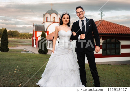 Interracial wedding couple smiling in front of a church Interracial wedding couple smiling in front of a church 133918417