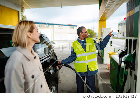 Service worker assisting woman refueling car at gas station Service worker assisting woman refueling car at gas station 133918428