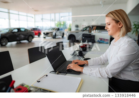 Car saleswoman typing on laptop in automotive dealership Car saleswoman typing on laptop in automotive dealership 133918446