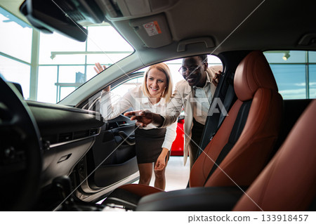 Salesperson showing car interior to customer in dealership 133918457
