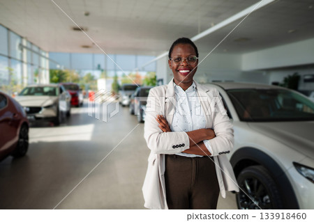 Happy woman sales manager standing in car dealership showroom Happy woman sales manager standing in car dealership showroom 133918460