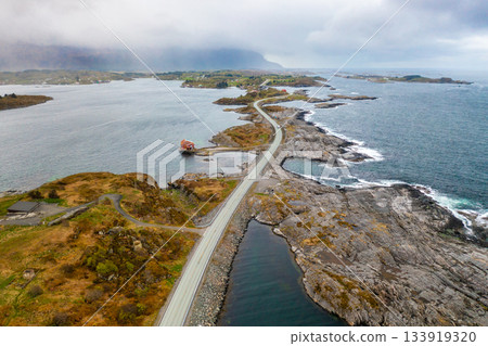 Atlantic ocean road snakes across small islands and skerries at dusk. Reflective water surface under cloudy sky highlights serene beauty of Norway 133919320