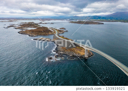 Dramatic span of Storseisundet Bridge forming a striking arch along the Atlantic Ocean Road, surrounded by sea and rocky islands of Norway 133919321