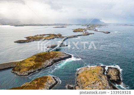 Winding Atlantic Ocean Road surrounded by waves and cliffs, capturing the raw power and serenity of Norways coastal scenery 133919328