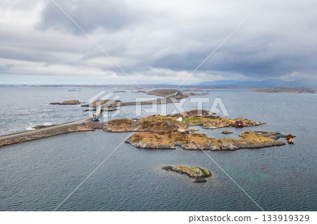 Atlantic ocean road gracefully arches over deep blue waters connecting Norwegian islets. Cars on bridge add striking pop of color under bright sky 133919329