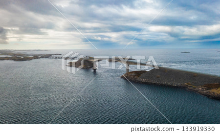 Dramatic Atlantic ocean road with iconic Storseisundet Bridge curves gracefully over turbulent water. Road connects islands and skerries in Norway 133919330