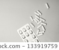 Many white pills scattered around a partially open pill blister pack on a flat surface 133919759
