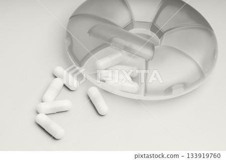 Pills spilling from a clear organizer on a white surface with a neat design 133919760