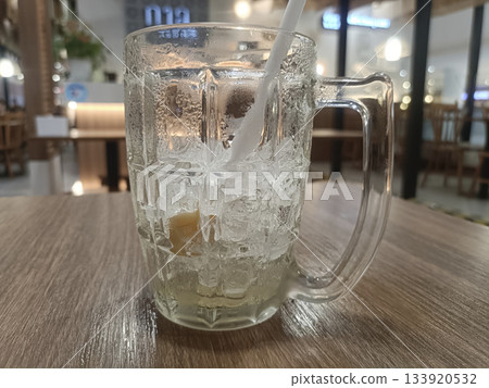 Iced glass mug clear beverage crushed ice straw lemon condensation cafe wooden table refreshment and calm vibe 133920532