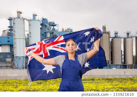 Sad young woman worker with flag of Australia against background of factory Sad young woman worker with flag of Australia against background of factory 133921610