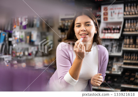 Positive girl testing new lipstick in cosmetics shop 133921618