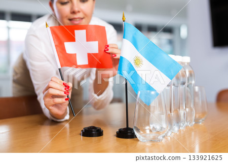 Preparing for business presentation - secretary places flags of Argentina and Switzerland on negotiating table 133921625